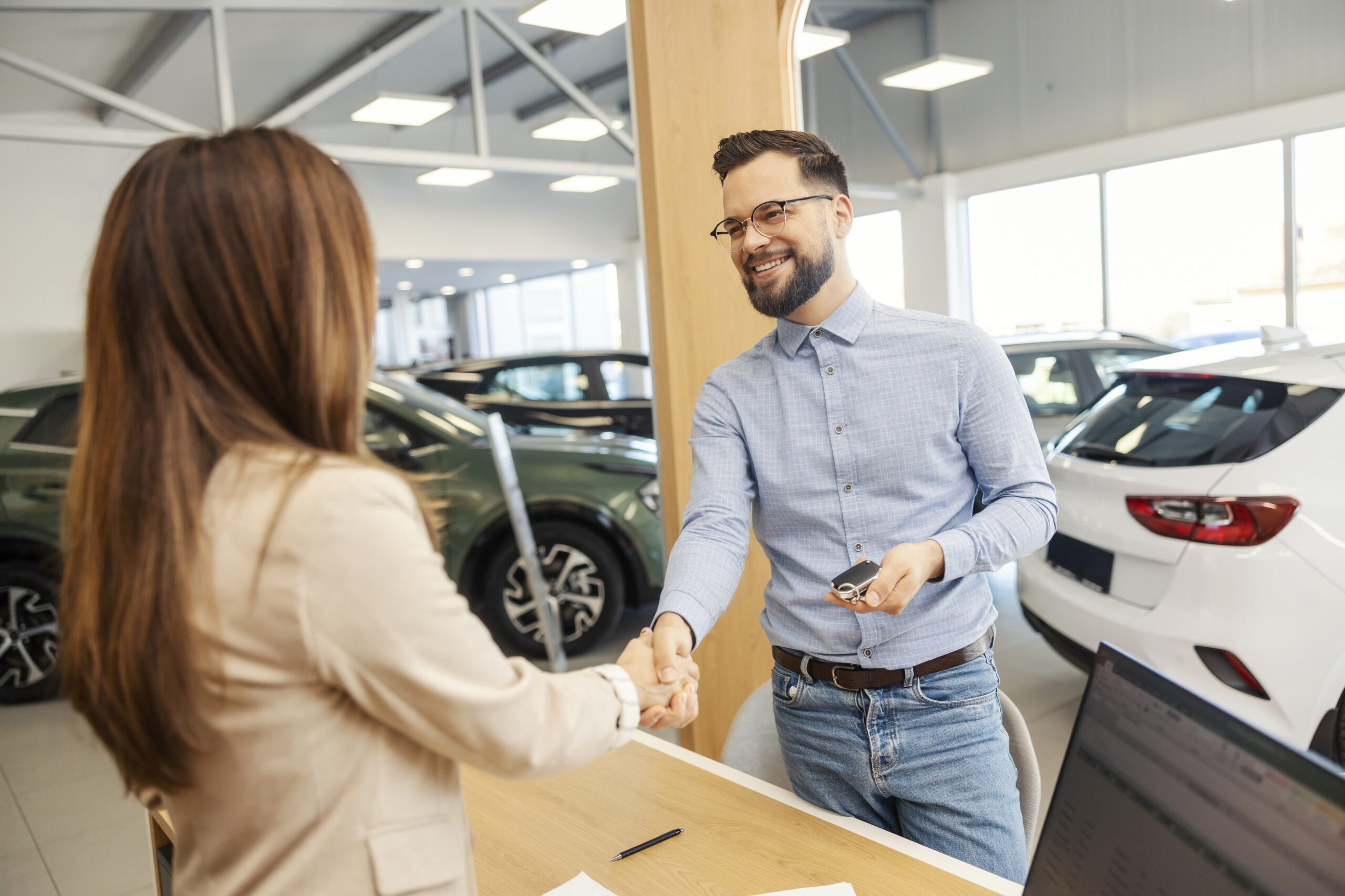 Happy customer with car keys in hand shaking hands with female car seller at car salon while closing the deal.