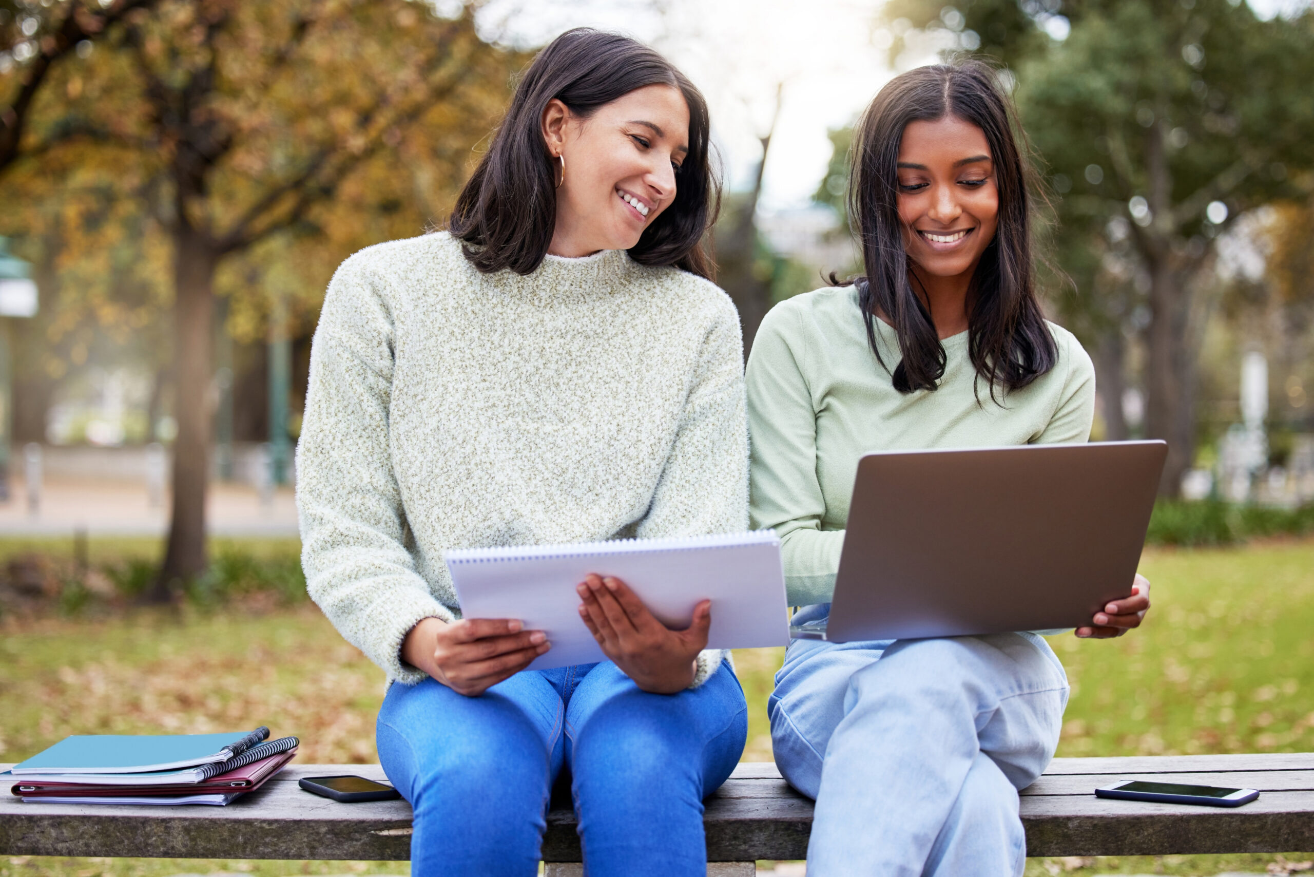 Students, laptop and friends in a park with learning, research and exam info on campus. Happy, school and university women with notes, online and college test with a computer outdoor on garden bench.